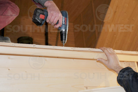 Screwing roofing boards into the log cabin wall